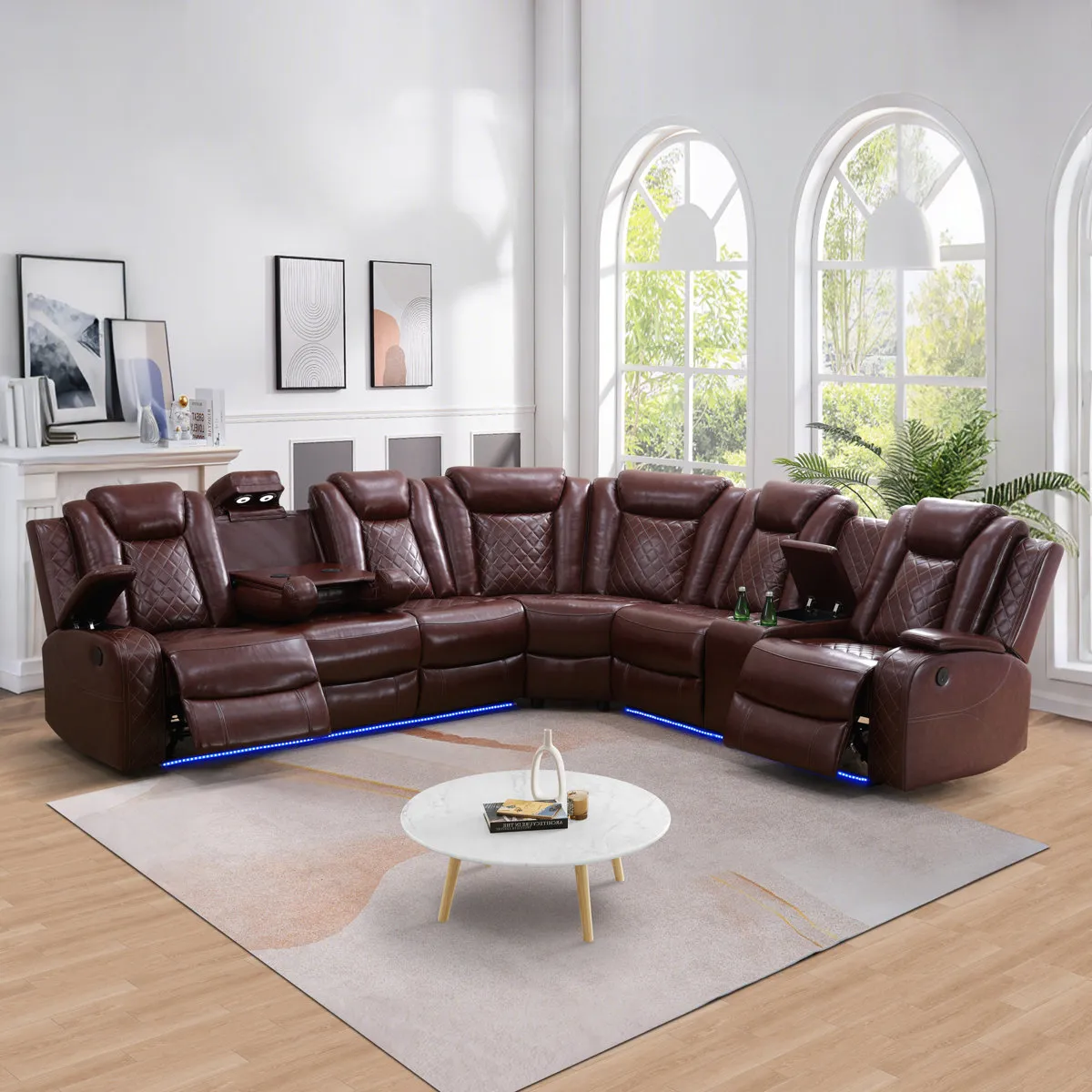 Brown leather sectional sofa with reclining seats and blue LED lighting, set in a room with white walls, large arched windows, and a small round marble table on a light-colored rug.