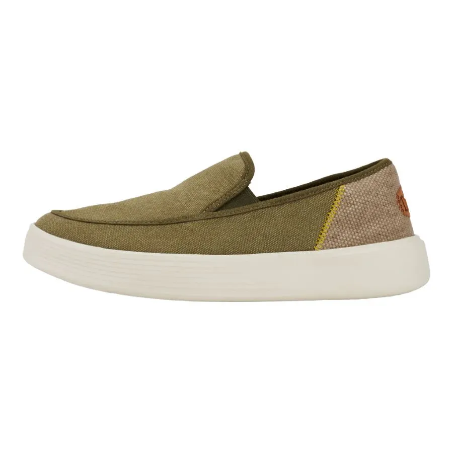 Olive green slip-on canvas shoe with a white sole and a small brown brand detail on the heel.