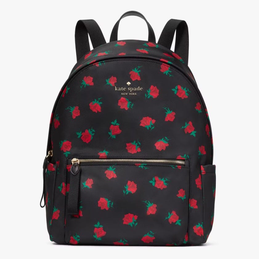 A black Kate Spade backpack with a red rose pattern and gold logo, featuring a front zip pocket and adjustable straps.
