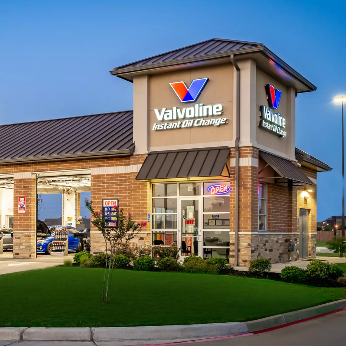 Valvoline Instant Oil Change service center with open garage bays showing cars inside, featuring a bright, modern exterior with illuminated signage and an \“open\“ sign.