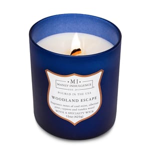 Blue glass candle labeled \“Manly Indulgence: Woodland Escape,\“ featuring fragrance notes of cool mint, Siberian pine, cypress, and tundra wood, 15 oz (425g).