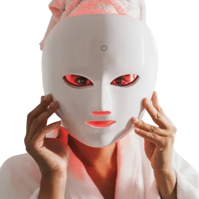 A person wearing an LED light therapy mask with a towel wrapped around their head, likely for skincare purposes.