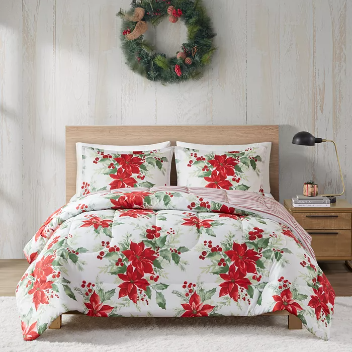 A festive bedding set with a red and green holly berry pattern, accompanied by a matching wreath hanging above the bed.