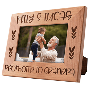 A wooden picture frame engraved with \“Kelly & Lucas Promoted to Grandpa,\“ featuring a photo of an older man joyfully lifting a baby.