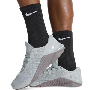 Nike black socks with white swoosh paired with light gray Nike Metcon shoes featuring a reinforced heel and mesh detailing.