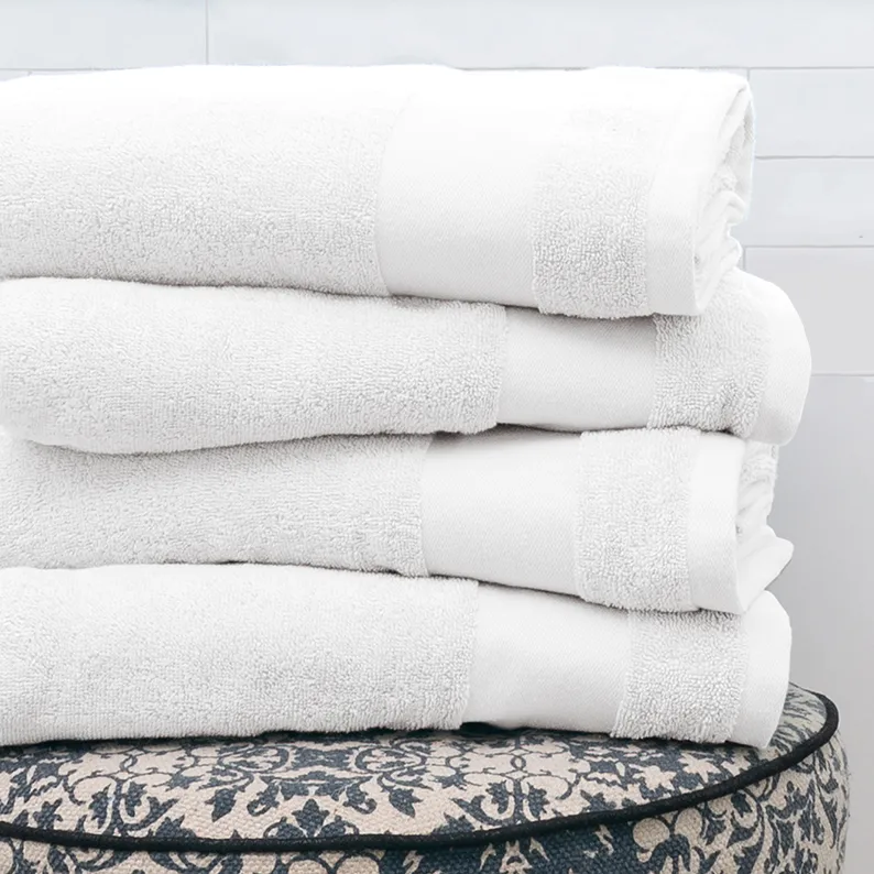 A stack of four plush, white bath towels is neatly folded, showcasing a luxurious texture and elegant design. They rest on a decorative surface with a black and white floral pattern.