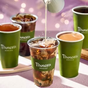Panera Bread cups filled with various drinks, including iced beverages and coffee, feature prominently. Milk is being poured into a clear cup with ice and coffee. All cups have the Panera Bread logo.