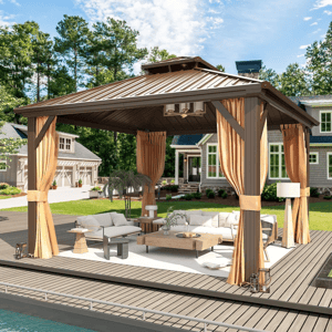 A backyard gazebo with a metal roof features tan curtains, patio furniture, and a wooden table on a deck by a pool, set in a residential garden with a house in the background.