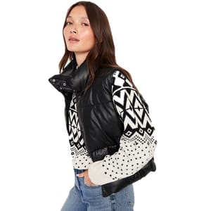 A woman is wearing a black puffer vest over a black and white geometric-patterned sweater paired with blue jeans.