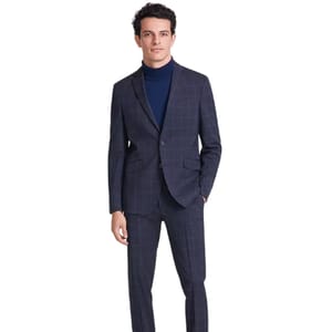 A man is wearing a Kenneth Cole Techni-Cole slim suit with a navy grid pattern. The outfit includes a tailored jacket and matching pants, paired with a dark blue turtleneck.