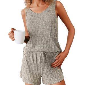 A person wearing a ribbed, sleeveless, gray lounge set with a tied waist, holding a white mug.