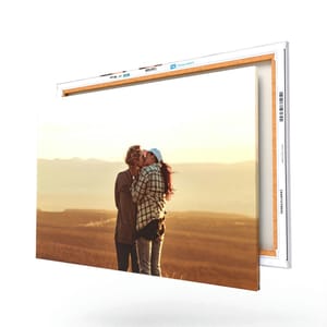 A canvas print displays two people kissing against a scenic backdrop, presented with a wooden frame edge.