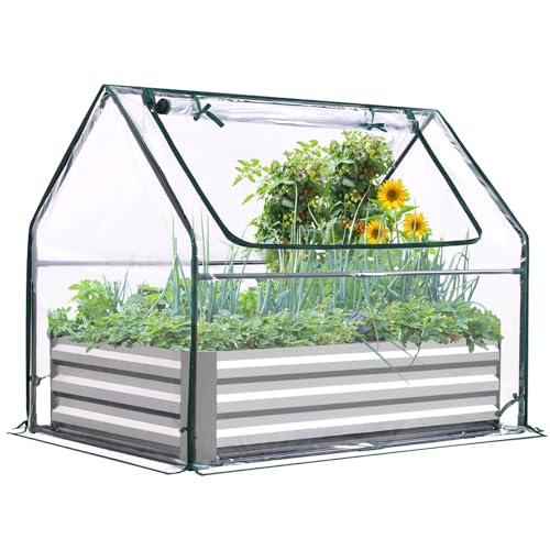 A small, clear plastic greenhouse with a metal frame covers a raised garden bed, containing various plants and flowers.