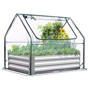 A small, clear plastic greenhouse with a metal frame covers a raised garden bed, containing various plants and flowers.