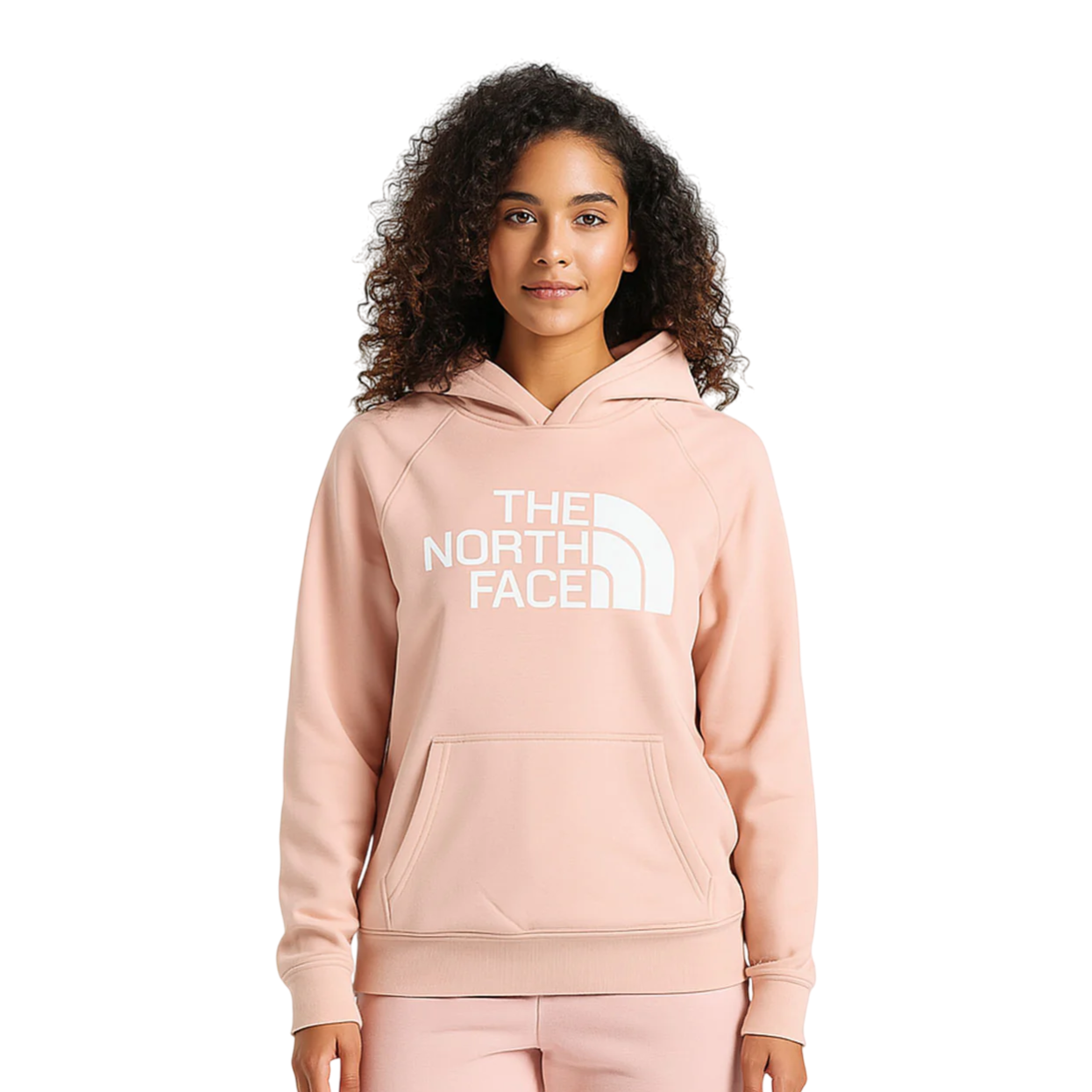 A woman wears a light pink hoodie with \“The North Face\“ logo in white, featuring a front pouch pocket and long sleeves.