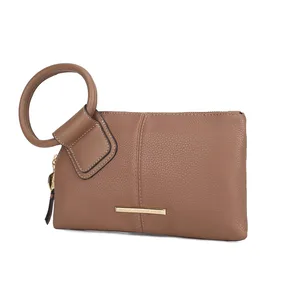 A tan wristlet clutch with a circular handle and gold-tone metal branding plaque.