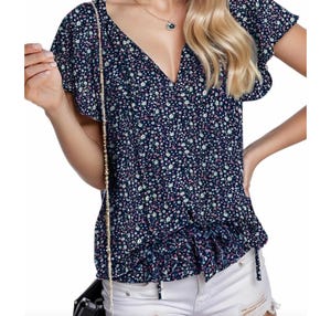 Floral ruffle-sleeve top with a V-neckline and tie details at the waist, in a navy blue base with white and pink flowers. Paired with white distressed shorts and a small black handbag.
