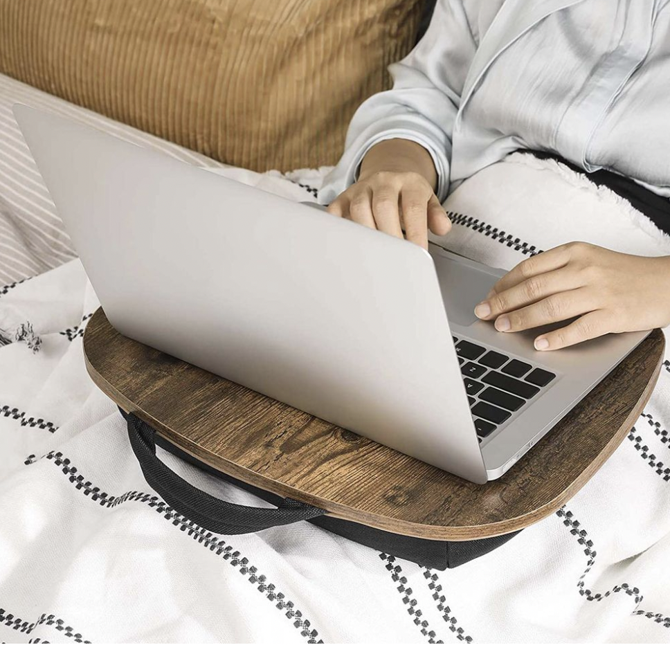 A wooden laptop table with a built-in handle. It provides a stable surface for using a laptop on a bed or couch, featuring a cushioned base for comfort and support.