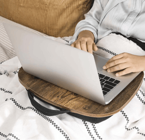 A wooden laptop table with a built-in handle. It provides a stable surface for using a laptop on a bed or couch, featuring a cushioned base for comfort and support.