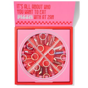 A pink and red pizza box contains JoyBright lip glosses arranged in a pizza slice pattern. The message inside the lid reads, \“It's all about who you want to eat pizza with at 2 am.\“