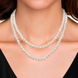 A woman is wearing a double-strand pearl necklace with white pearls, paired with a black top.