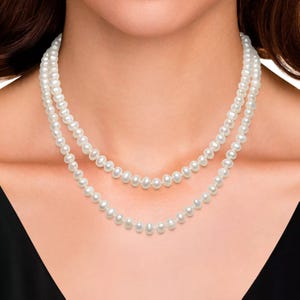 A woman is wearing a double-strand pearl necklace with white pearls, paired with a black top.