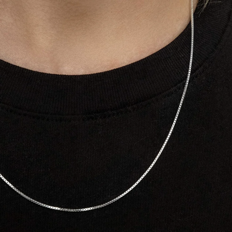 A silver box chain necklace rests on a black shirt, offering a minimalist and elegant design suitable for everyday wear.