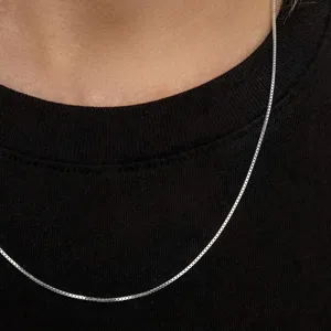 A silver box chain necklace rests on a black shirt, offering a minimalist and elegant design suitable for everyday wear.