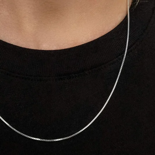 A silver box chain necklace rests on a black shirt, offering a minimalist and elegant design suitable for everyday wear.