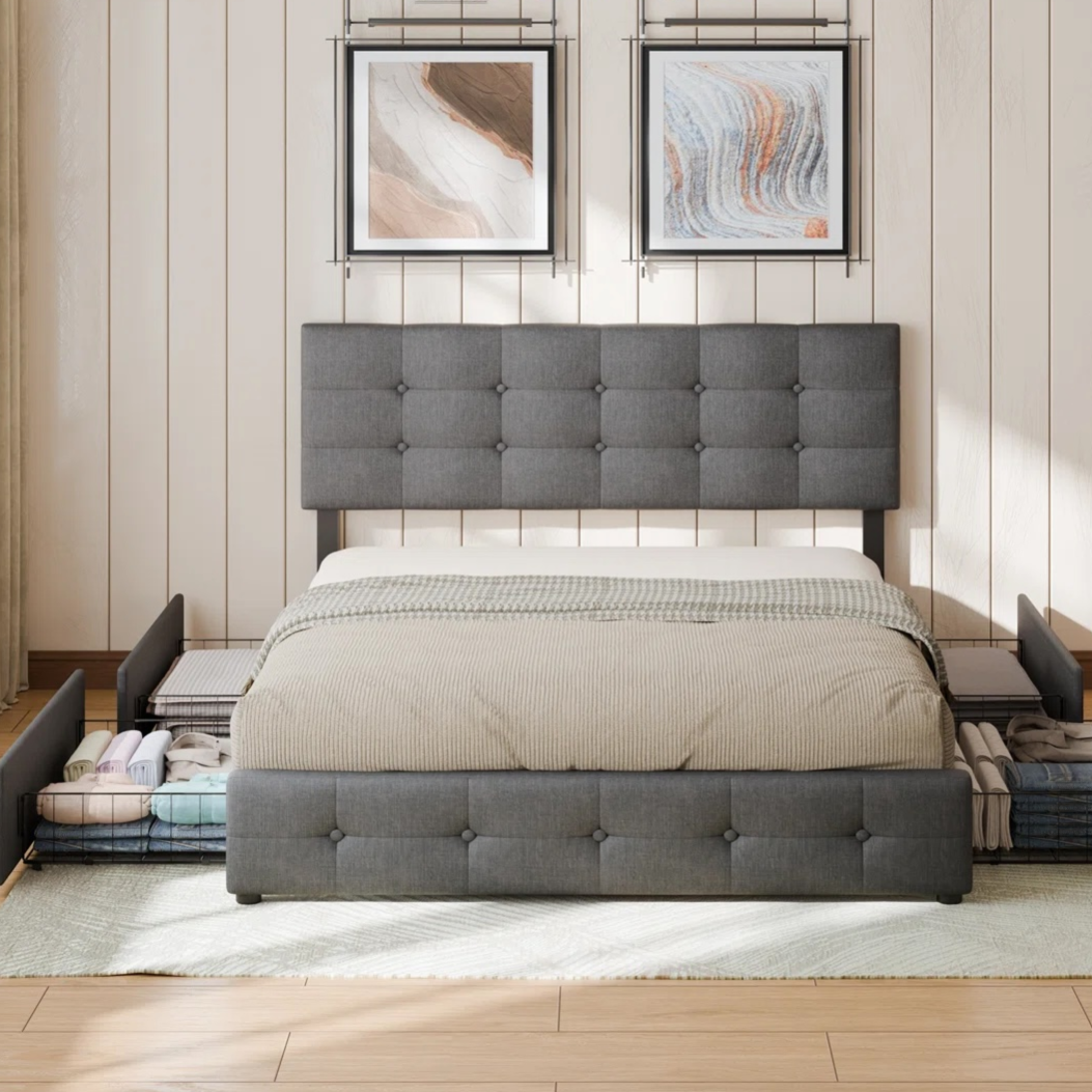 A modern gray tufted bed features built-in storage drawers on the sides and footboard, ideal for organizing linens. It is set against a light wood-paneled wall with abstract art and illuminated by a ceiling chandelier.