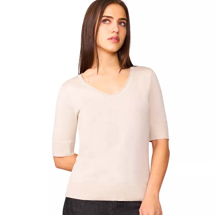 A woman wears a light beige, short-sleeved, V-neck sweater paired with dark pants.