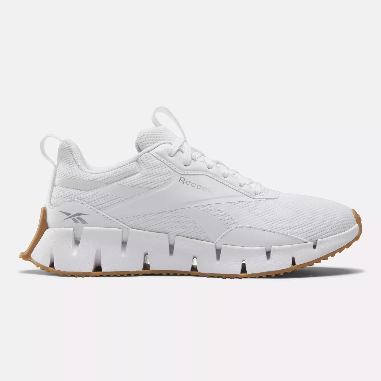 White Reebok Zig Dynamica shoes with a distinctive zigzag-shaped, jagged sole in a contrasting gum color.