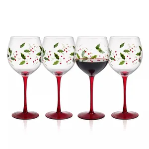 Set of four wine glasses with red stems, adorned with holly and berry designs. One glass is filled with red wine.