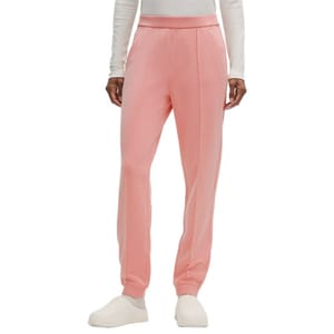 A person wears pink pleated pants paired with a long-sleeved white top and off-white slip-on shoes.