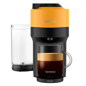 A yellow and black Nespresso espresso machine with a compact design featuring a clear water tank and a glass cup of espresso beneath the spout.