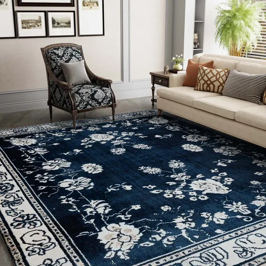 A living room features a beige sofa with patterned cushions, a patterned armchair, and a blue floral rug.