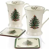 Two ceramic mugs and two coasters, each featuring a Christmas tree design with green borders and mistletoe accents.