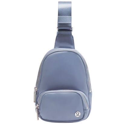 A small, light blue sling bag with a single adjustable strap and multiple zippered compartments, featuring a logo emblem on the front.