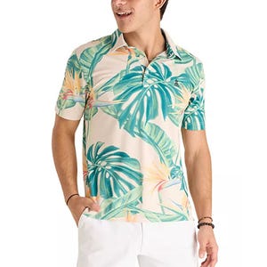 A man is wearing a short-sleeved, tropical-patterned polo shirt with palm leaves, paired with white shorts.
