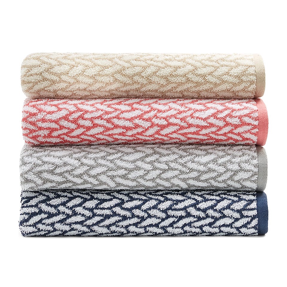 Four rolled towels with a chevron pattern in beige, pink, gray, and navy colors are stacked neatly.