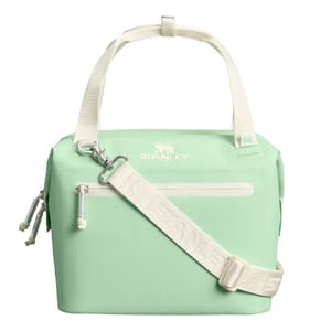 A mint green Stanley lunch cooler bag with a white adjustable shoulder strap and handles, featuring a front zipper pocket and a zippered closure on top.