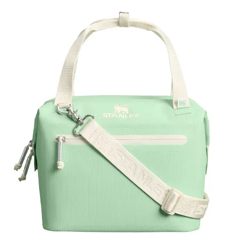 A mint green Stanley lunch cooler bag with a white adjustable shoulder strap and handles, featuring a front zipper pocket and a zippered closure on top.