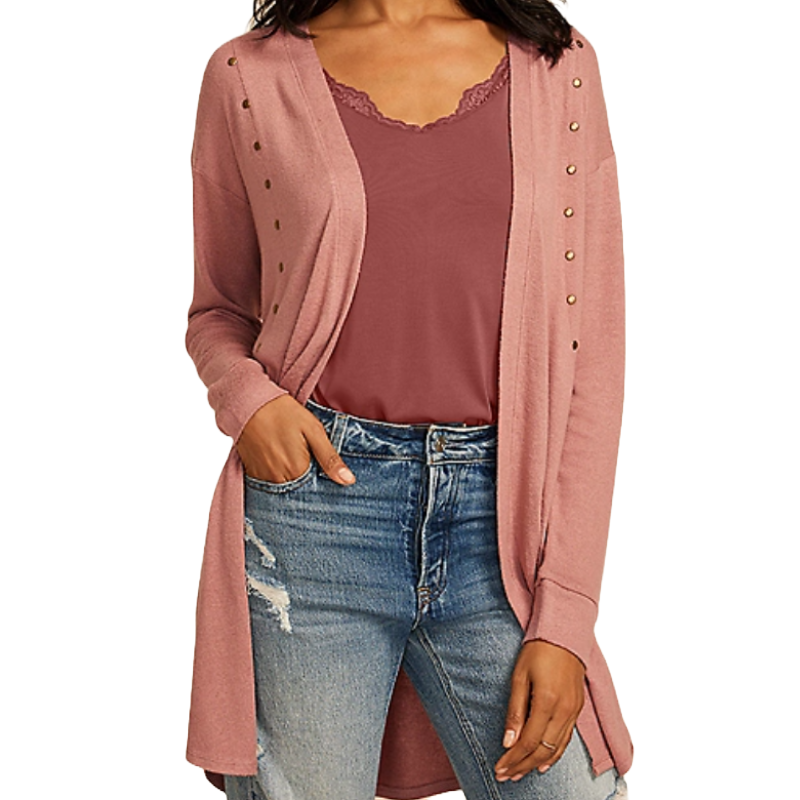 A woman is wearing a dusty pink open-front cardigan with metal studs over a lace-trimmed maroon top, paired with distressed blue jeans.