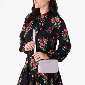 Woman wearing a black floral dress holds a small light-colored shoulder bag.