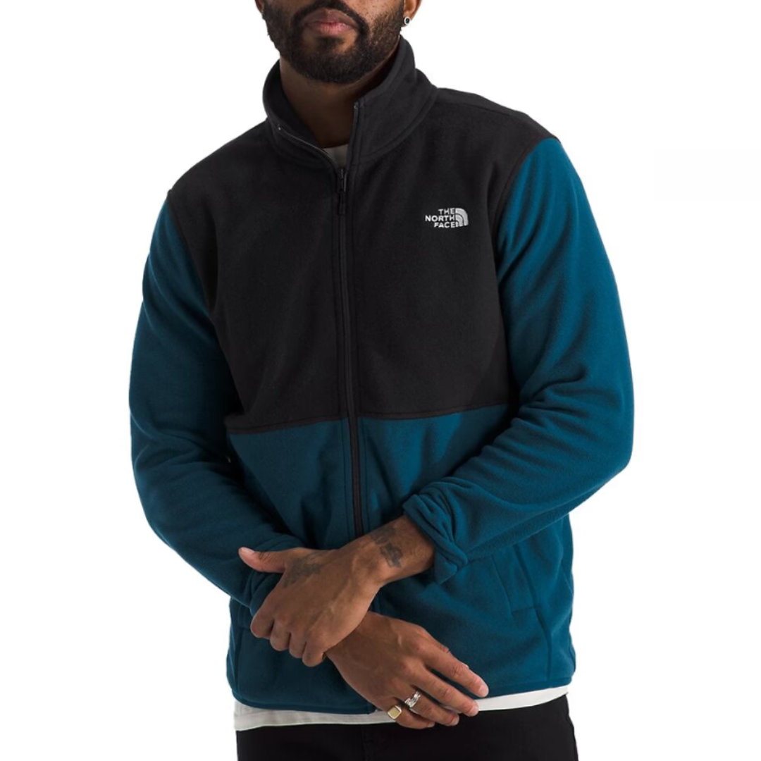 The North Face Glacier Fleece features a two-tone design with a black upper section and teal blue lower section. It has a full zip front, stand-up collar, and the logo is visible on the chest.