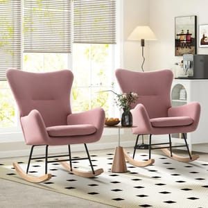 Two pink upholstered rocking chairs with wooden runners are positioned in a bright room near a window. A small round table with a vase and snacks sits between them on a patterned rug.