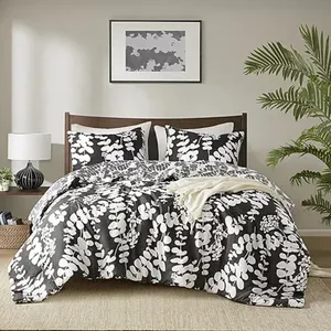 A bed features a black and white floral-patterned comforter set, with matching pillows. The room includes a lamp on a side table, framed abstract art above the bed, and a potted plant on the right.