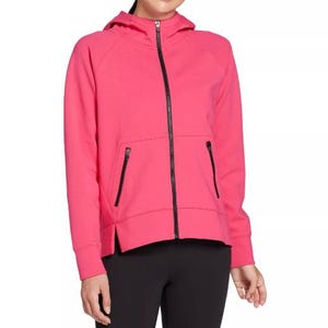 A woman is wearing a bright pink zip-up hooded sweatshirt with black zipper accents and front pockets, paired with black leggings.
