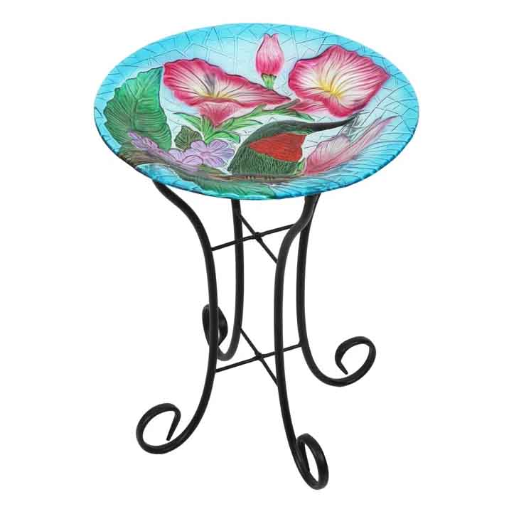 Glass birdbath featuring a vibrant floral pattern with pink and purple flowers on a turquoise background, supported by a black metal folding stand with decorative scrollwork.
