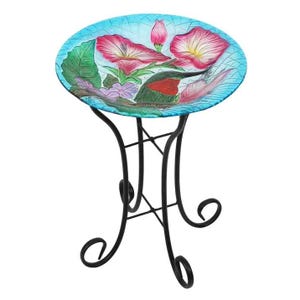 Glass birdbath featuring a vibrant floral pattern with pink and purple flowers on a turquoise background, supported by a black metal folding stand with decorative scrollwork.